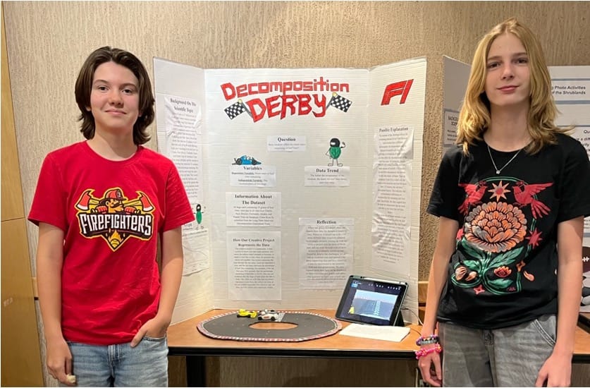 Sierra Middle School students Lucy Smart and Oliver Mason stand beside their “Decomposition Derby” Desert Data Jam project display.