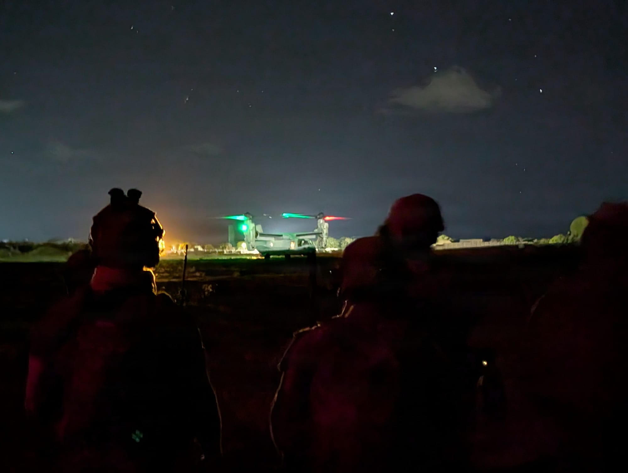 Silhouetted service members stand near a U.S. Marine Corps MV-22B Osprey aircraft preparing for takeoff at night in East Africa.