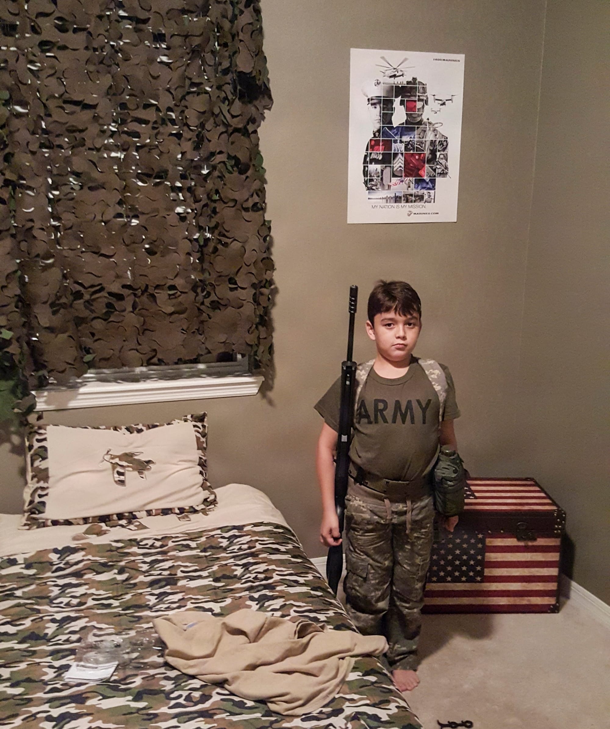 A young Nicolas Ferrari stands in a military-themed bedroom wearing camouflage clothing and an “ARMY” shirt while holding a toy rifle in 2015.