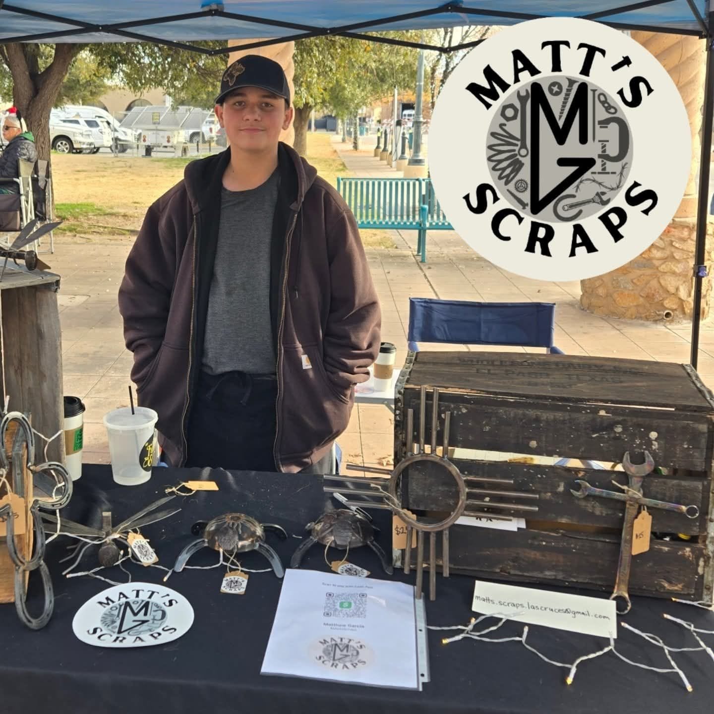 Matthew Garcia stands behind a table displaying handmade metal items at a market booth labeled Matt’s Scraps.