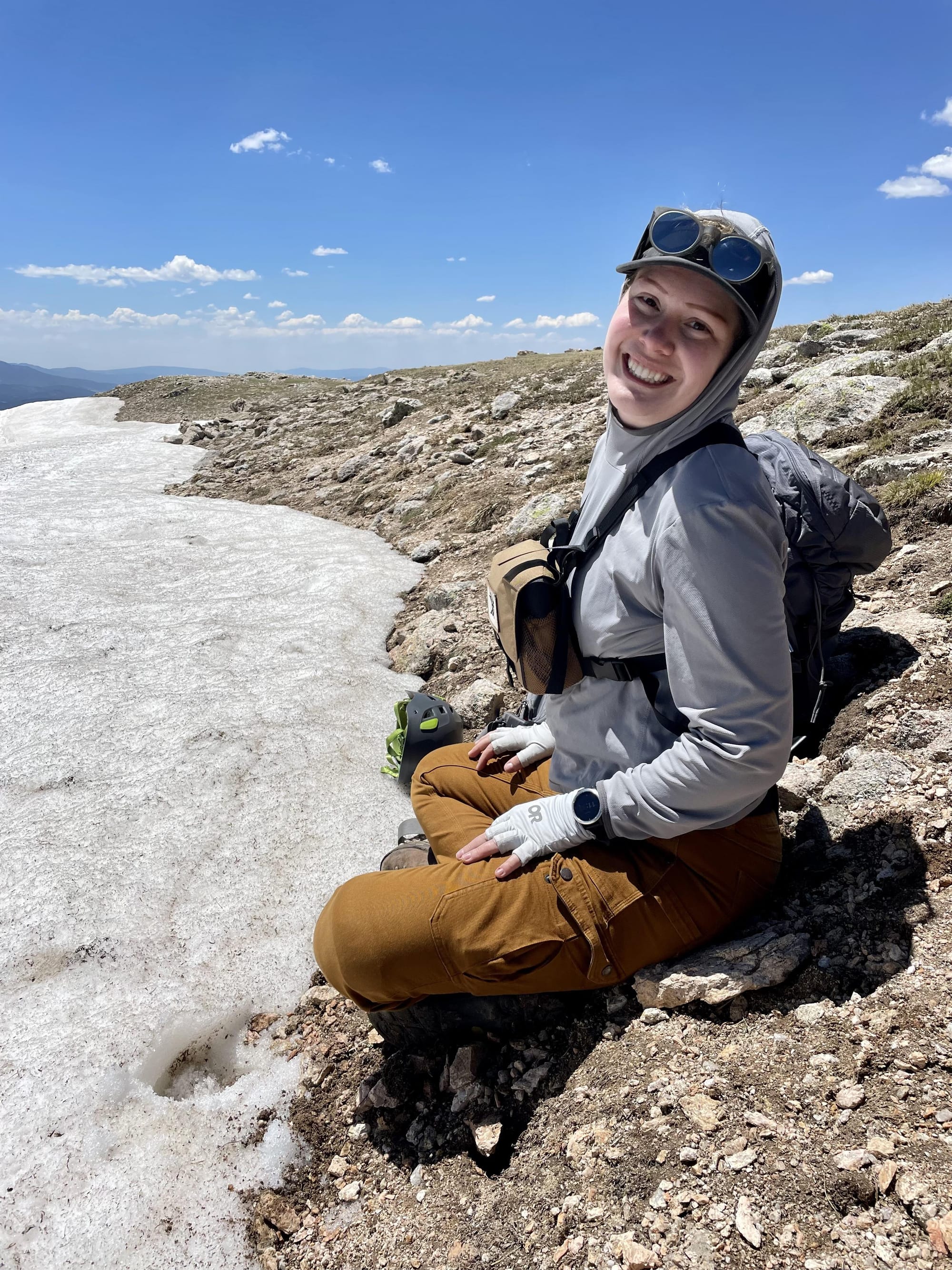 NMSU doctoral student Whitney Watson sits on a rocky mountainside near a snowfield during field research at Vermejo Park Ranch.