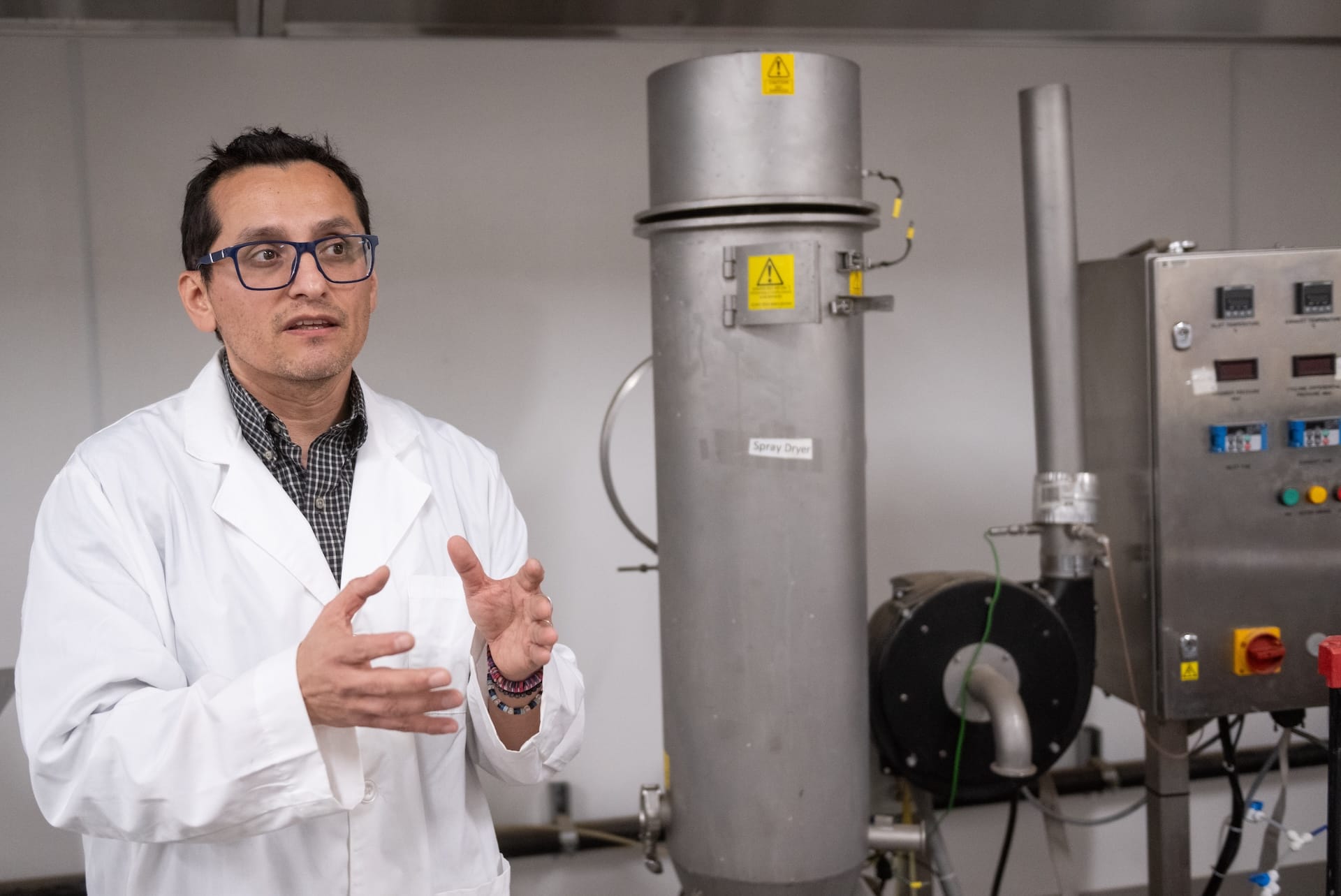 New Mexico State University researcher Sergio Martinez-Monteagudo gestures while standing beside food-processing equipment in a campus laboratory.