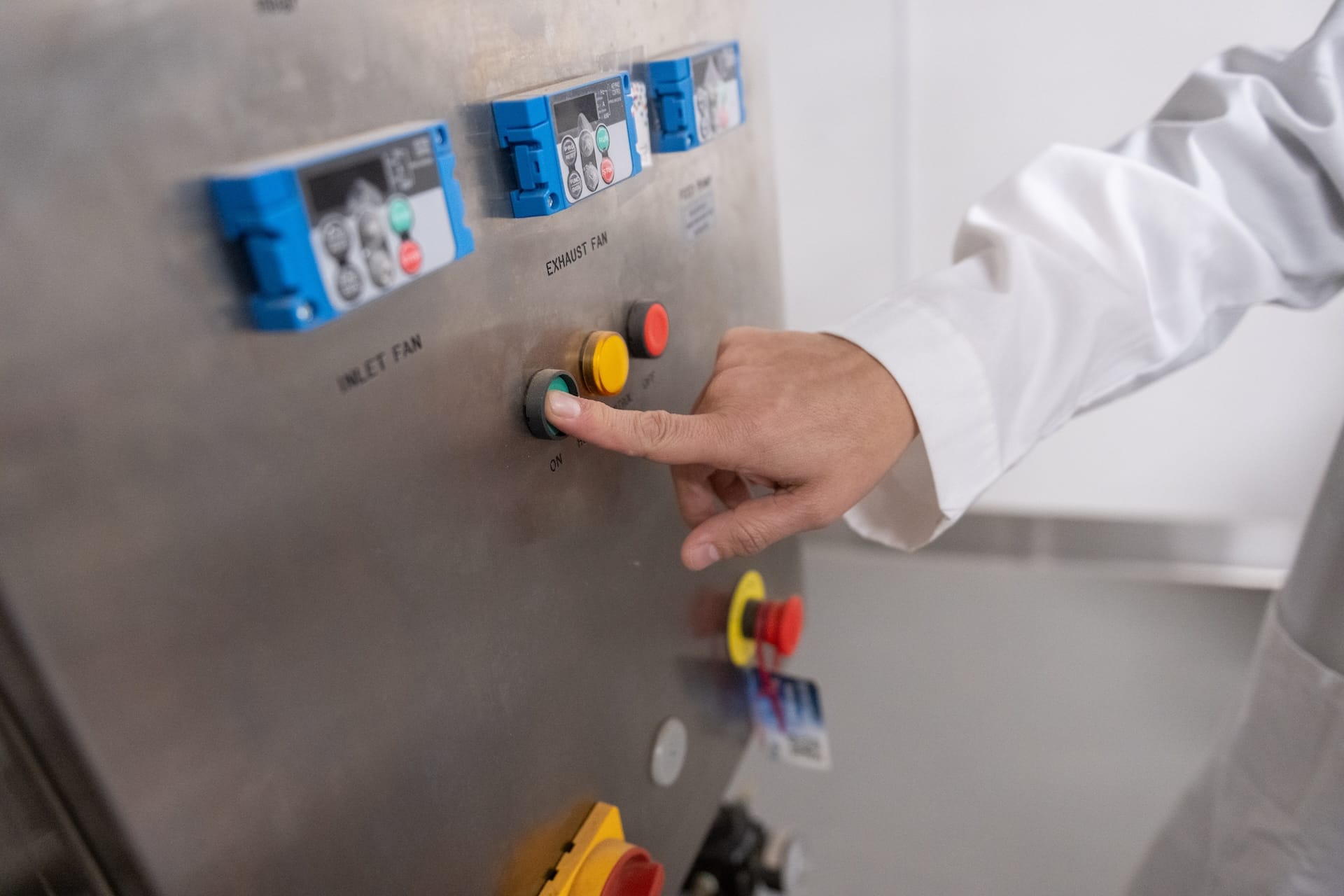 A researcher wearing a white lab coat presses a green start button on the control panel of food-processing equipment in an NMSU laboratory.