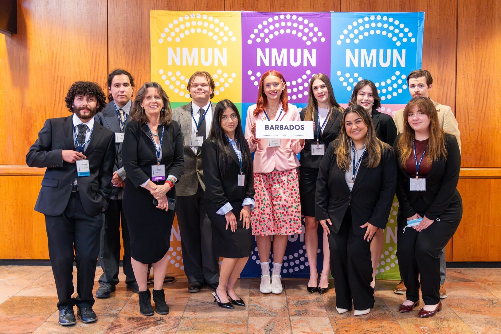 Group of New Mexico State University Model United Nations students and faculty posing at a conference, with one student holding a sign labeled “Barbados” in front of NMUN banners.
