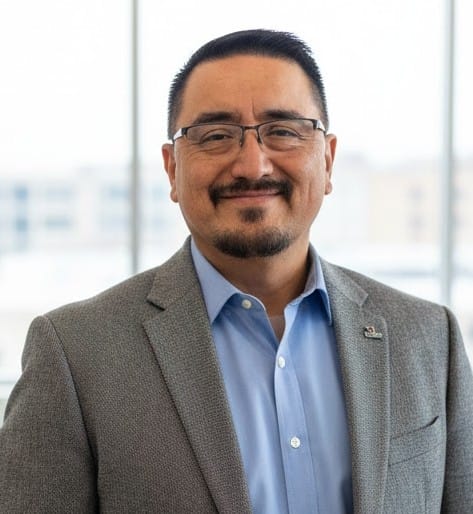 Democratic Doña Ana County sheriff candidate Rafael Reyes Jr. poses for a portrait wearing glasses, a blue shirt and gray blazer.