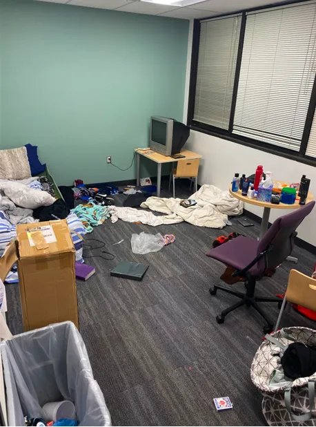 A cluttered office room at a CYFD building in Albuquerque, where foster youth were sleeping, with bedding on the floor, scattered belongings and a small television on a table.