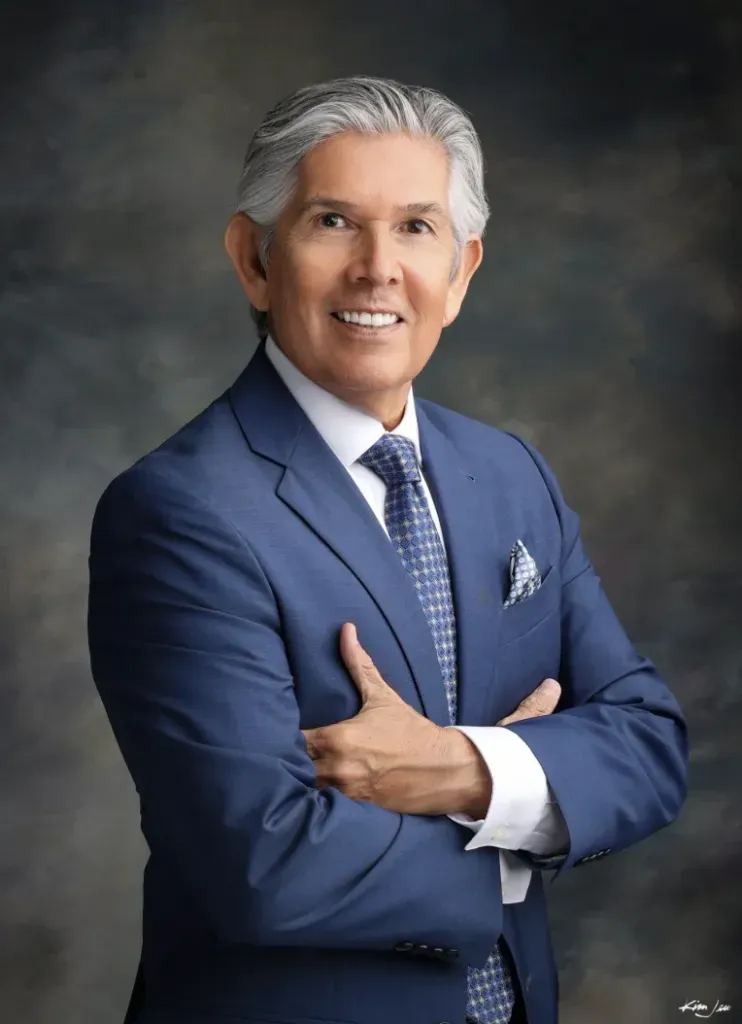 Portrait of Duke Rodriguez, a New Mexico gubernatorial candidate, wearing a blue suit and tie with arms crossed.