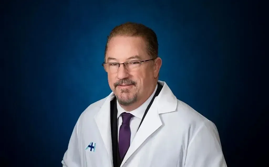 Dr. Peter Jewell poses for a portrait wearing a white medical coat.
