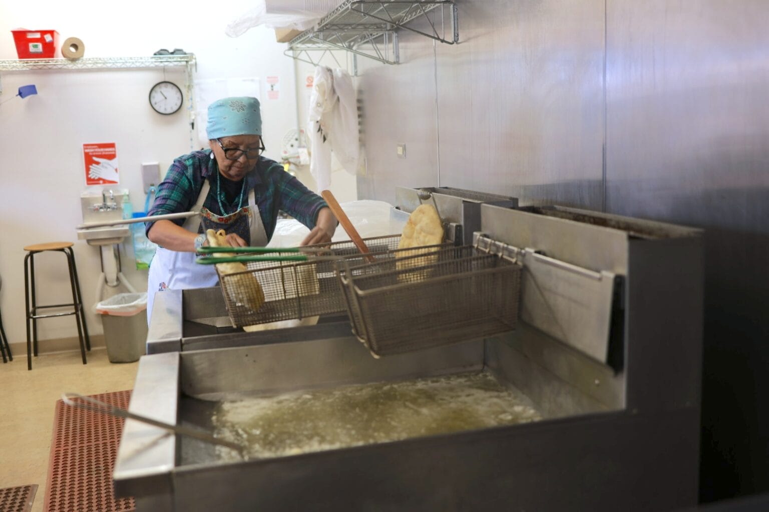 A kitchen worker places food into a deep fryer in a commercial kitchen during food preparation.