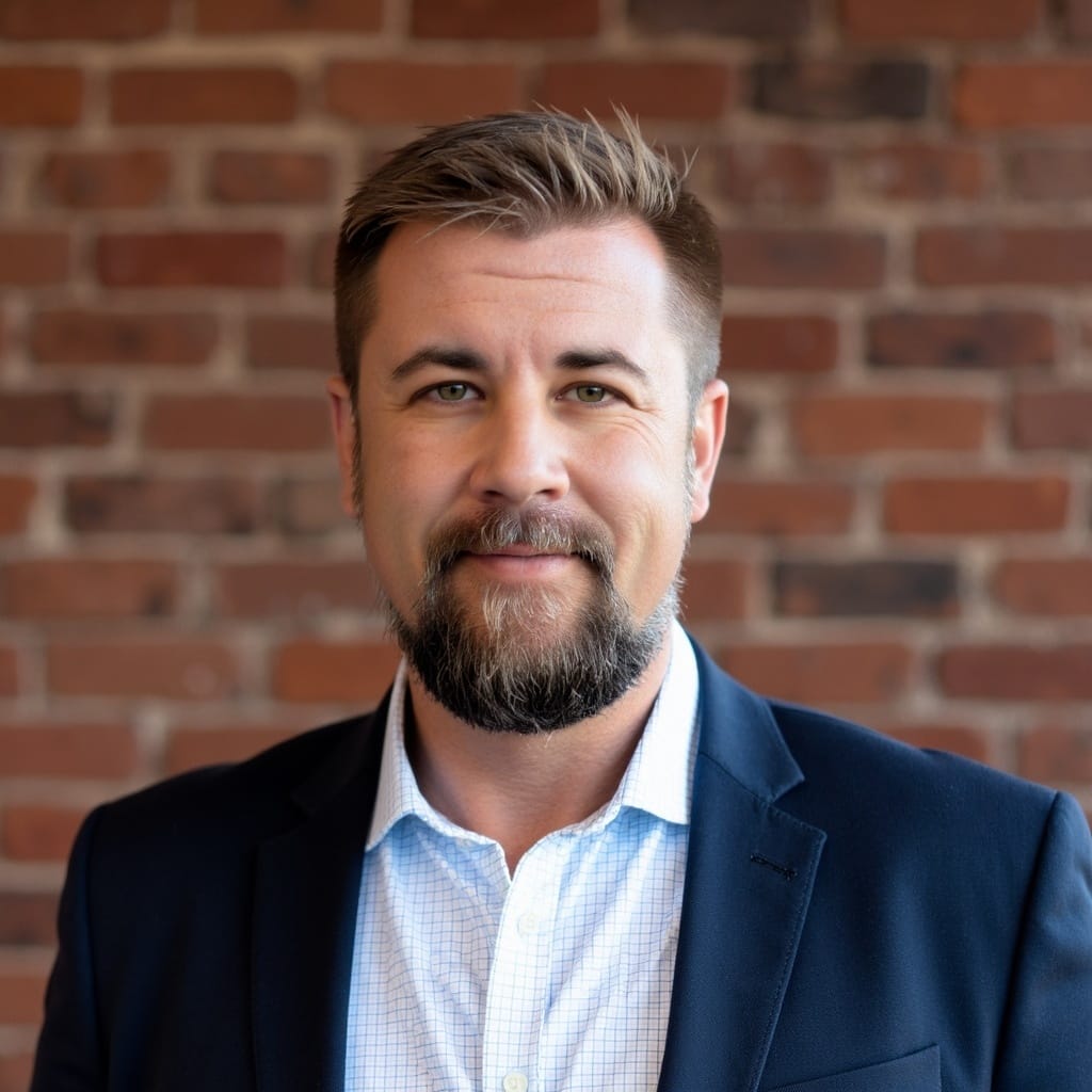 Portrait of Aubrey Blair Dunn in a suit and collared shirt, standing in front of a brick wall.