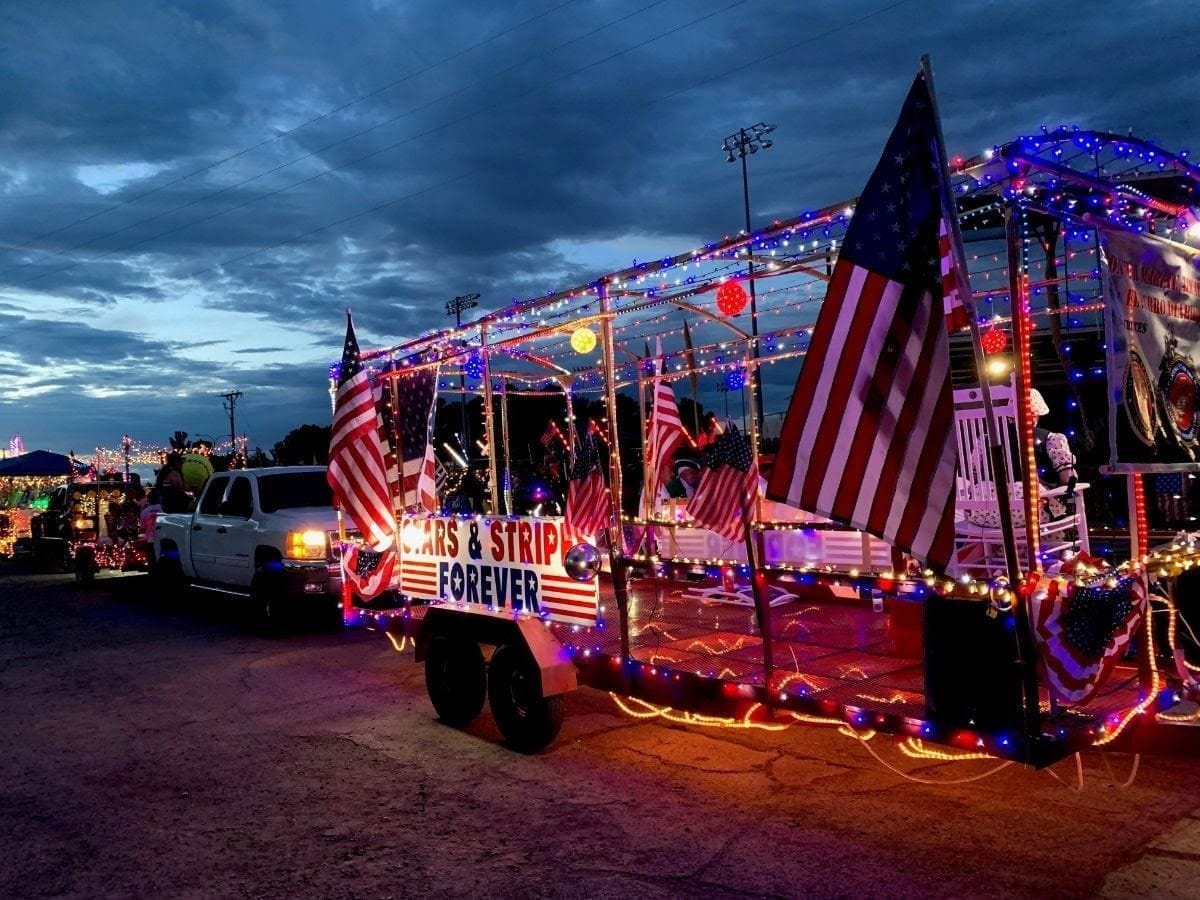 A Fourth of July parade float covered in red, white and blue lights and American flags travels at dusk in Las Cruces.