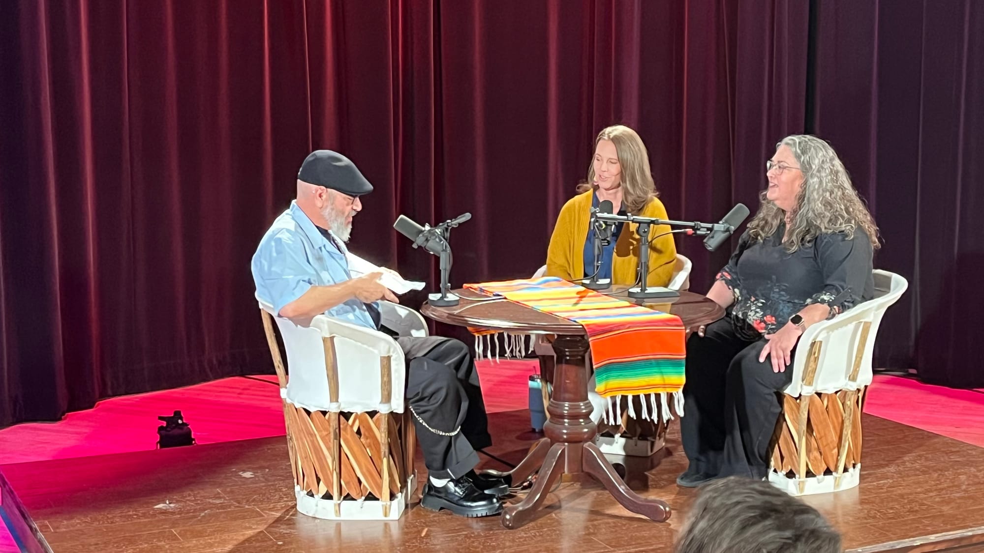 Manuel González, seated at left, speaks with Terra Winter and Mary Ulrich around a table with microphones during a live “Pass the Sopapillas” taping at KRWG Studios.