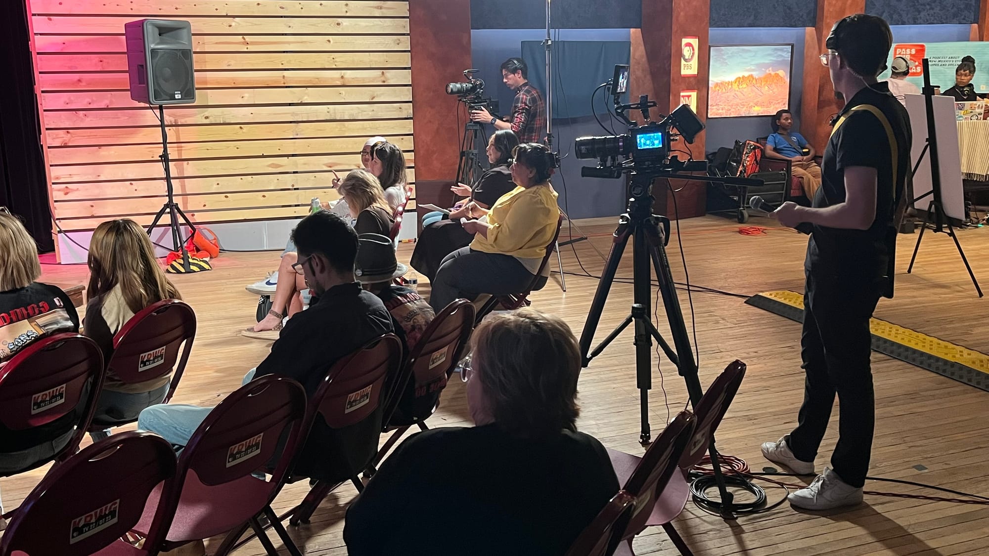Attendees sit facing the stage during a live “Pass the Sopapillas” taping at KRWG Studios, with video cameras and production equipment positioned in the room.