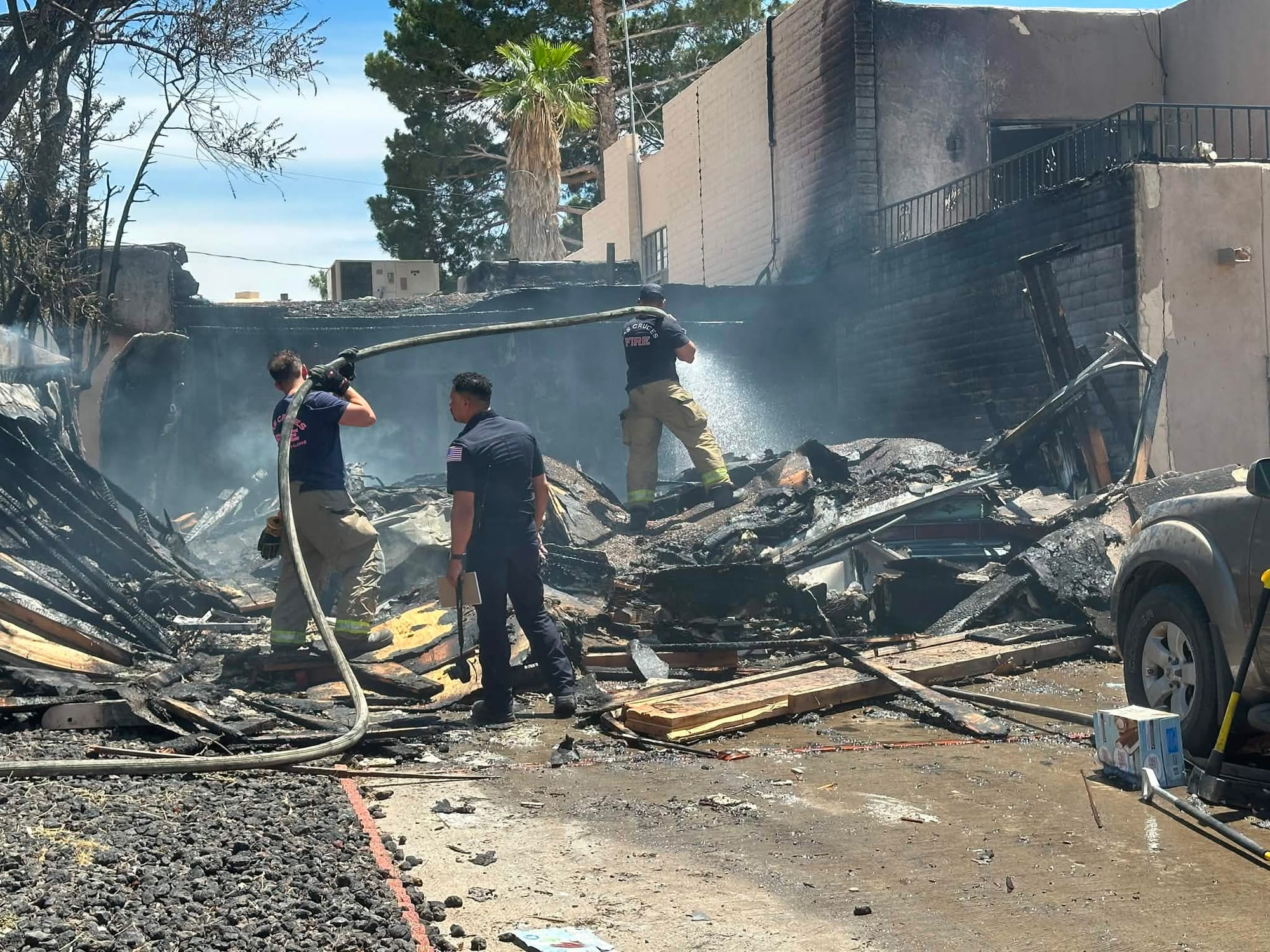 Three Las Cruces firefighters stand amid burned debris while spraying water at the scene of a residential explosion and fire on Fairway Drive.