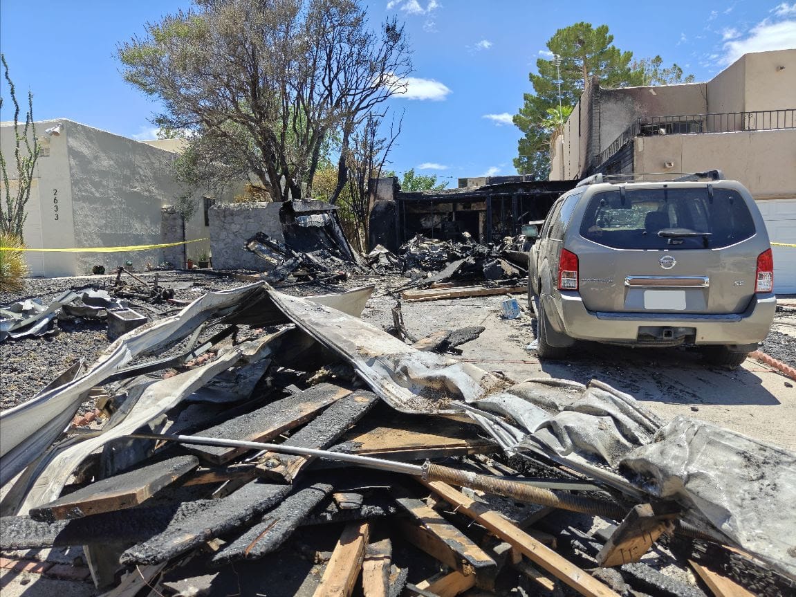 Fire and explosion damage outside a Fairway Drive residence in Las Cruces, with burned debris, a scorched garage area and a damaged SUV in the driveway.