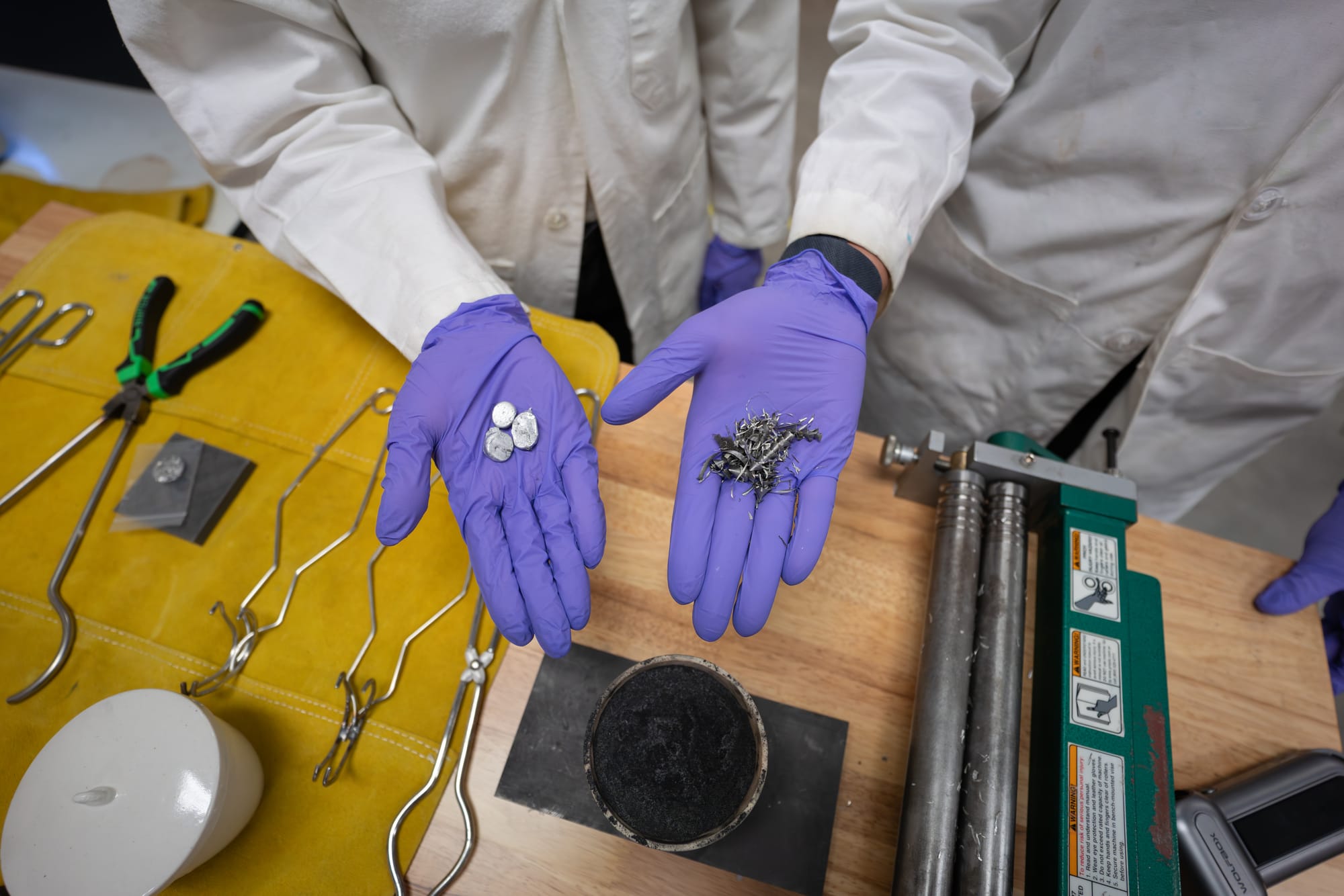 Two hands hold scrap metal parts in a lab where they melt and reuse scrap metal.