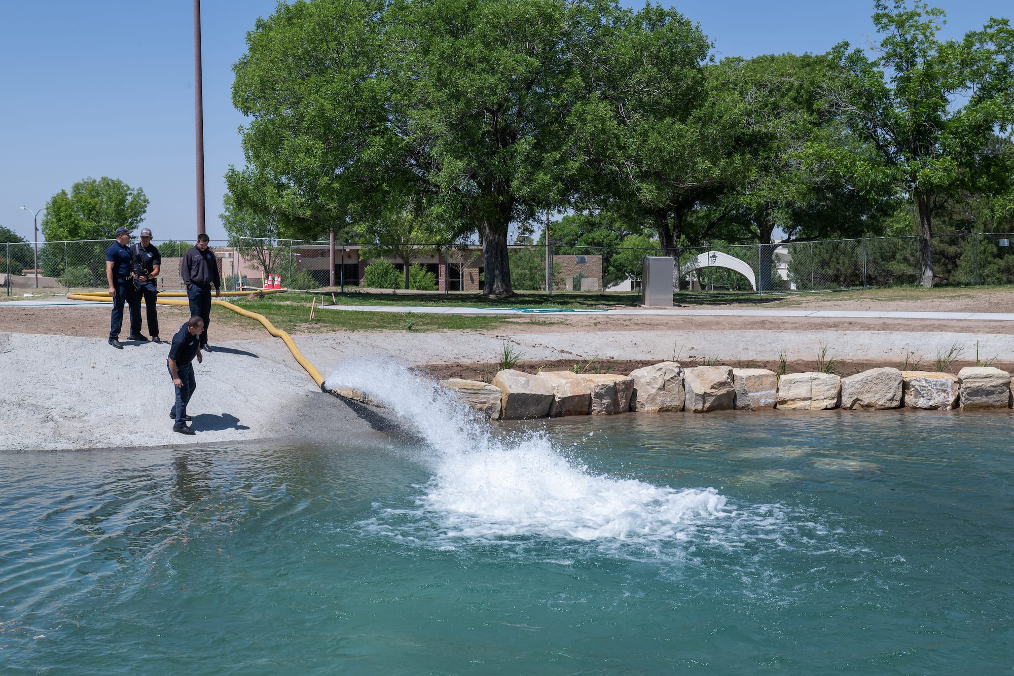 Three workers monitor a hose discharging water into the renovated Alumni Pond at New Mexico State University.