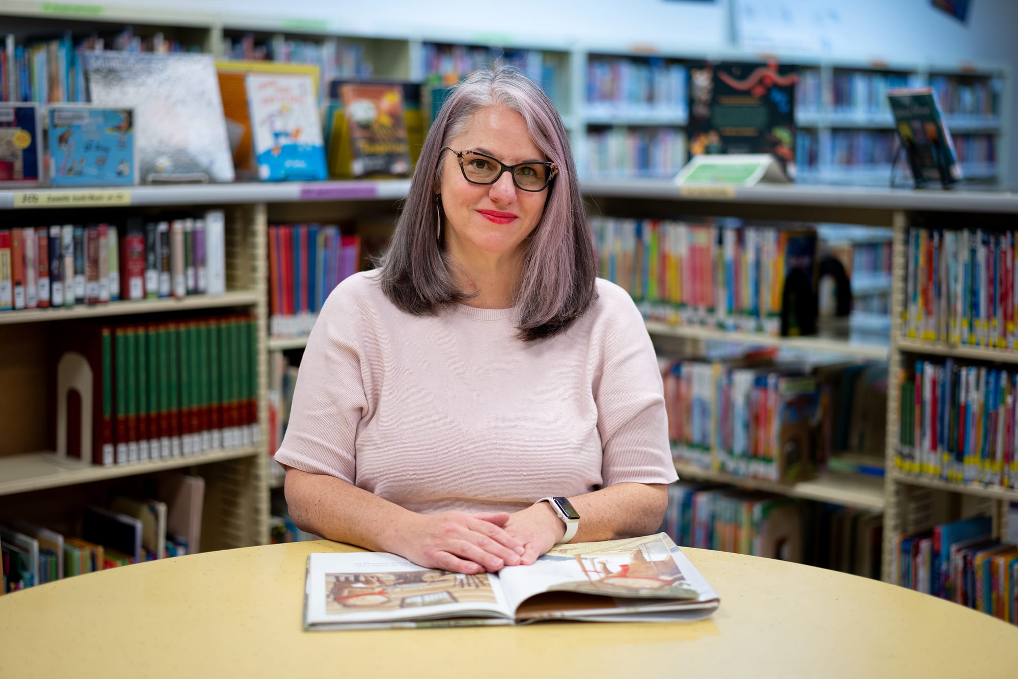 Nancy Stephens sits at a library table with an open children’s book in front of her.
