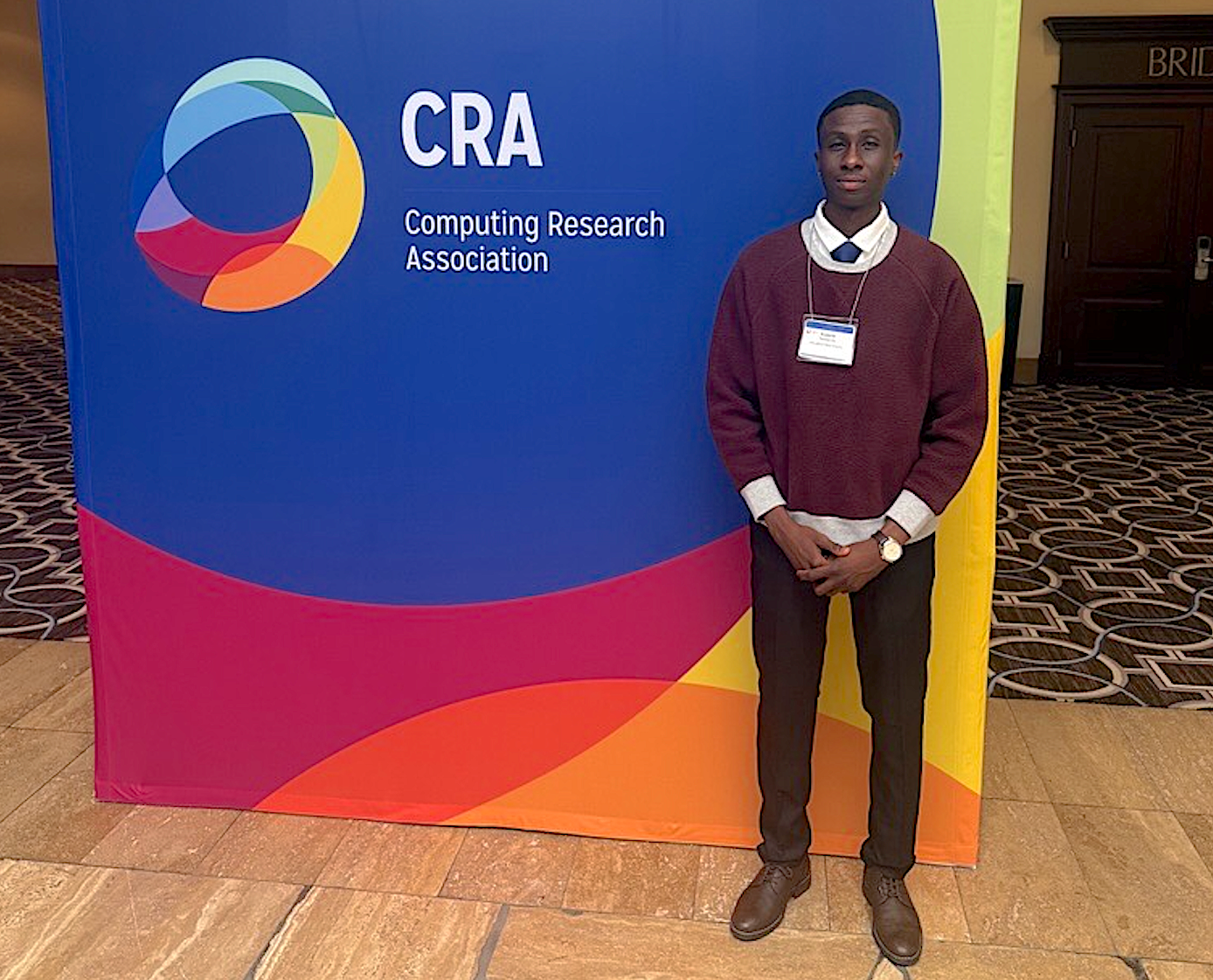 NMSU computer science student Eugene Taabazuing stands beside a Computing Research Association sign at the UR2PhD workshop in New Orleans.