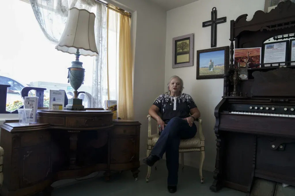 Las Cruces advocate Yoli Diaz sits in a chair in her office between an antique desk and organ, with framed artwork and a cross on the wall behind her.