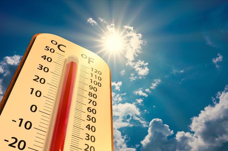 A close-up thermometer shows temperatures above 100 degrees Fahrenheit beneath a bright sun and blue sky.