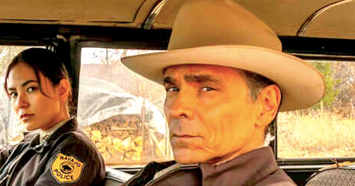 Zahn McClarnon and Jessica Matten, in Navajo Tribal Police uniforms, sit inside a vehicle in a scene from AMC's Dark Winds.