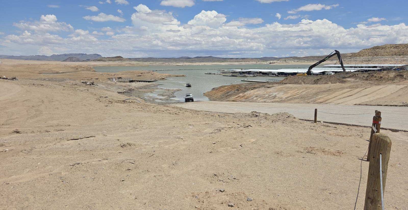A boat ramp extends toward the receding shoreline at Elephant Butte Lake as low water levels expose surrounding lakebed and crews work nearby.