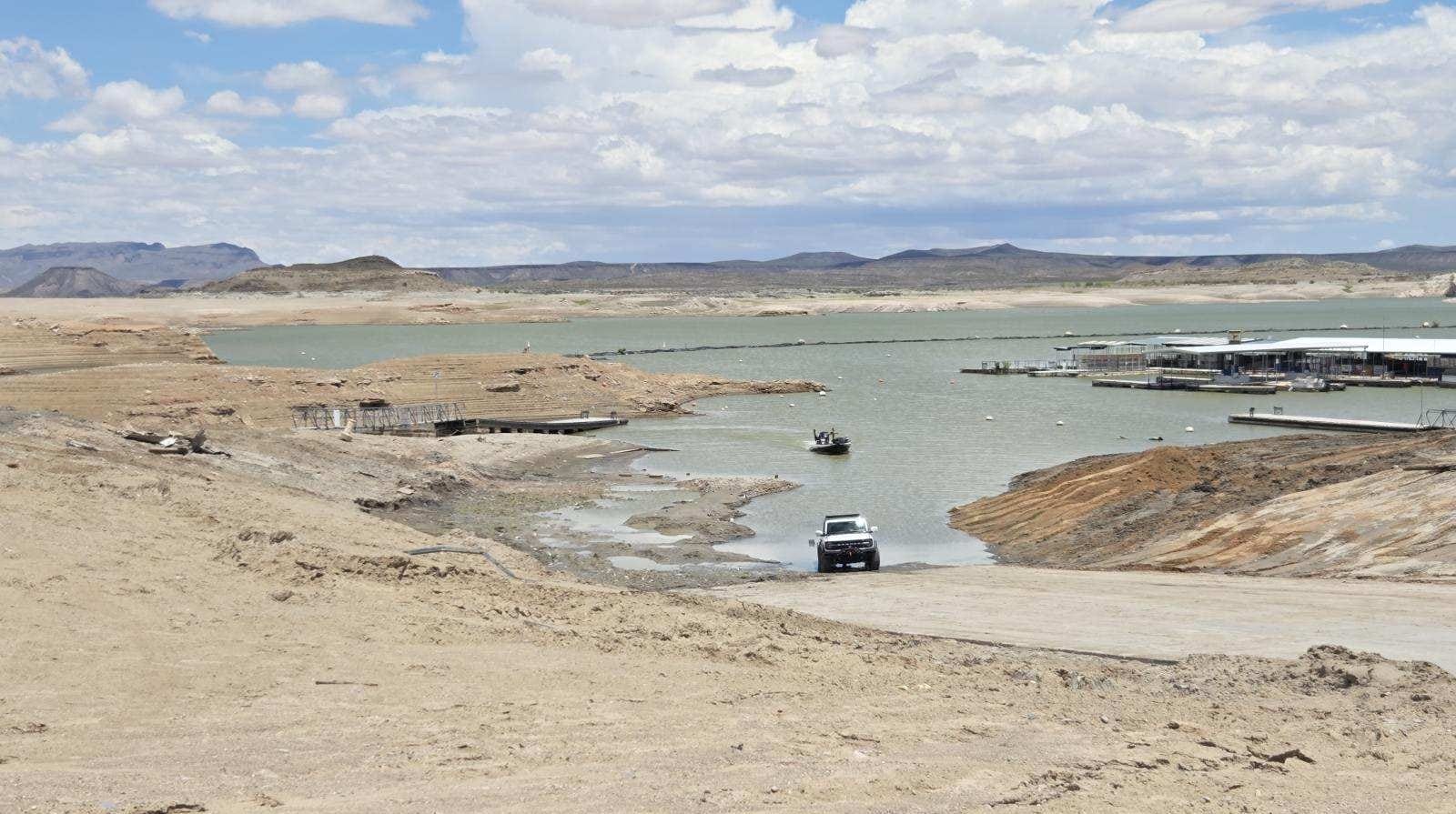 A pickup truck and small boat navigate low water near the Marina del Sur boat ramp at Elephant Butte Lake, where receding water has exposed large sections of shoreline.