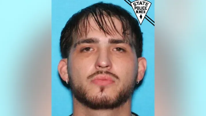 Booking-style photo of Dominic De La O against a blue background, with a New Mexico State Police logo in the upper right.