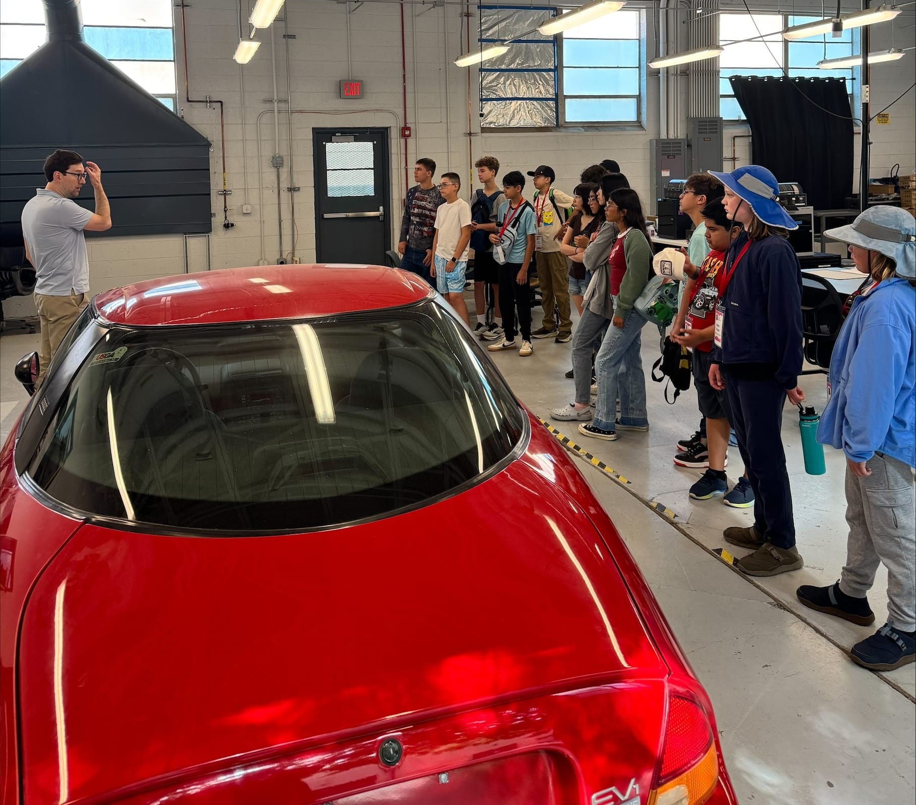 Middle school students attending NM PREP Academy are gathered around a red electric car in a mechanical engineering lab while they listen to an instructor.