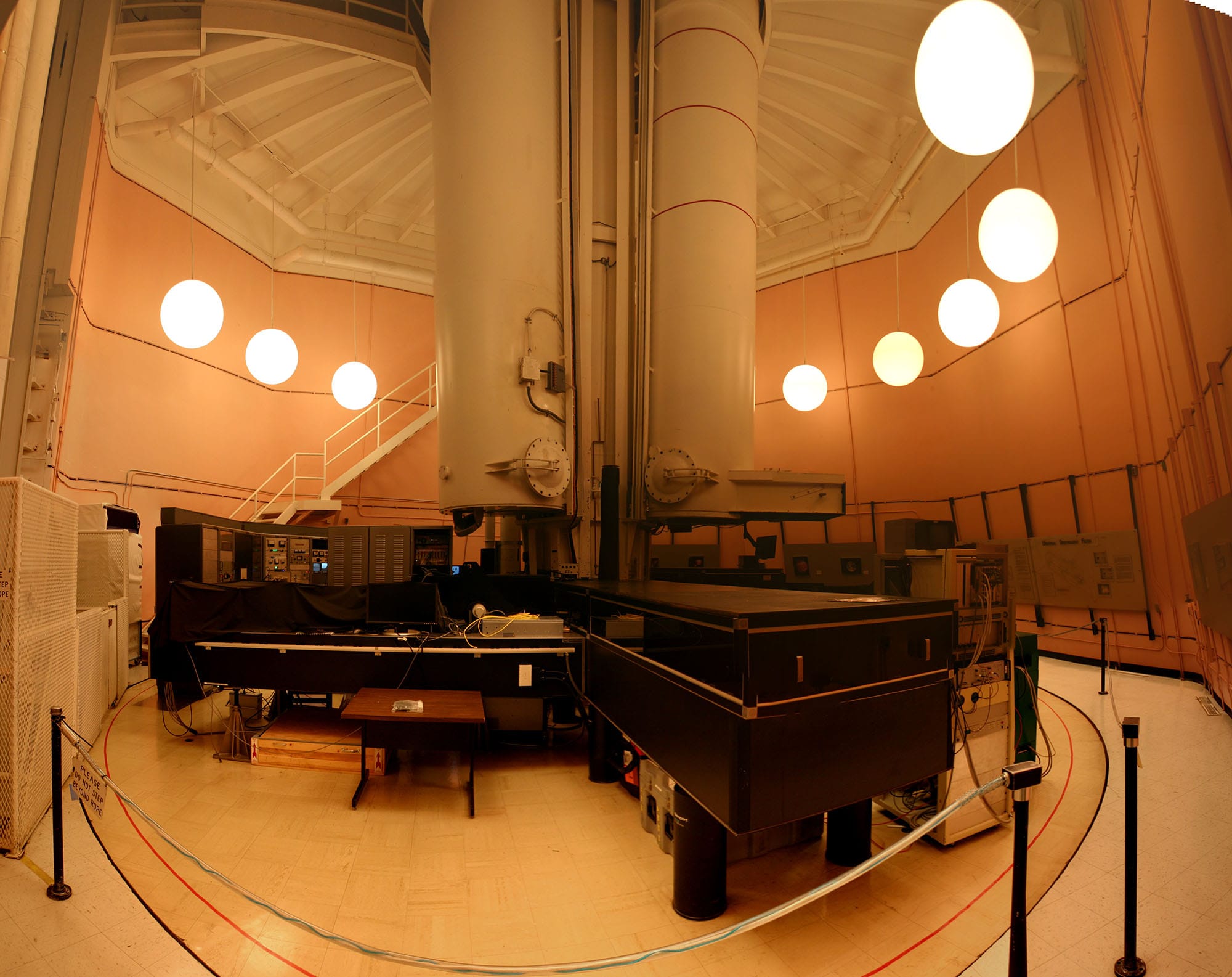 Inside the Richard B. Dunn Solar Telescope, large white telescope columns rise above equipment tables in an orange-walled observatory room.