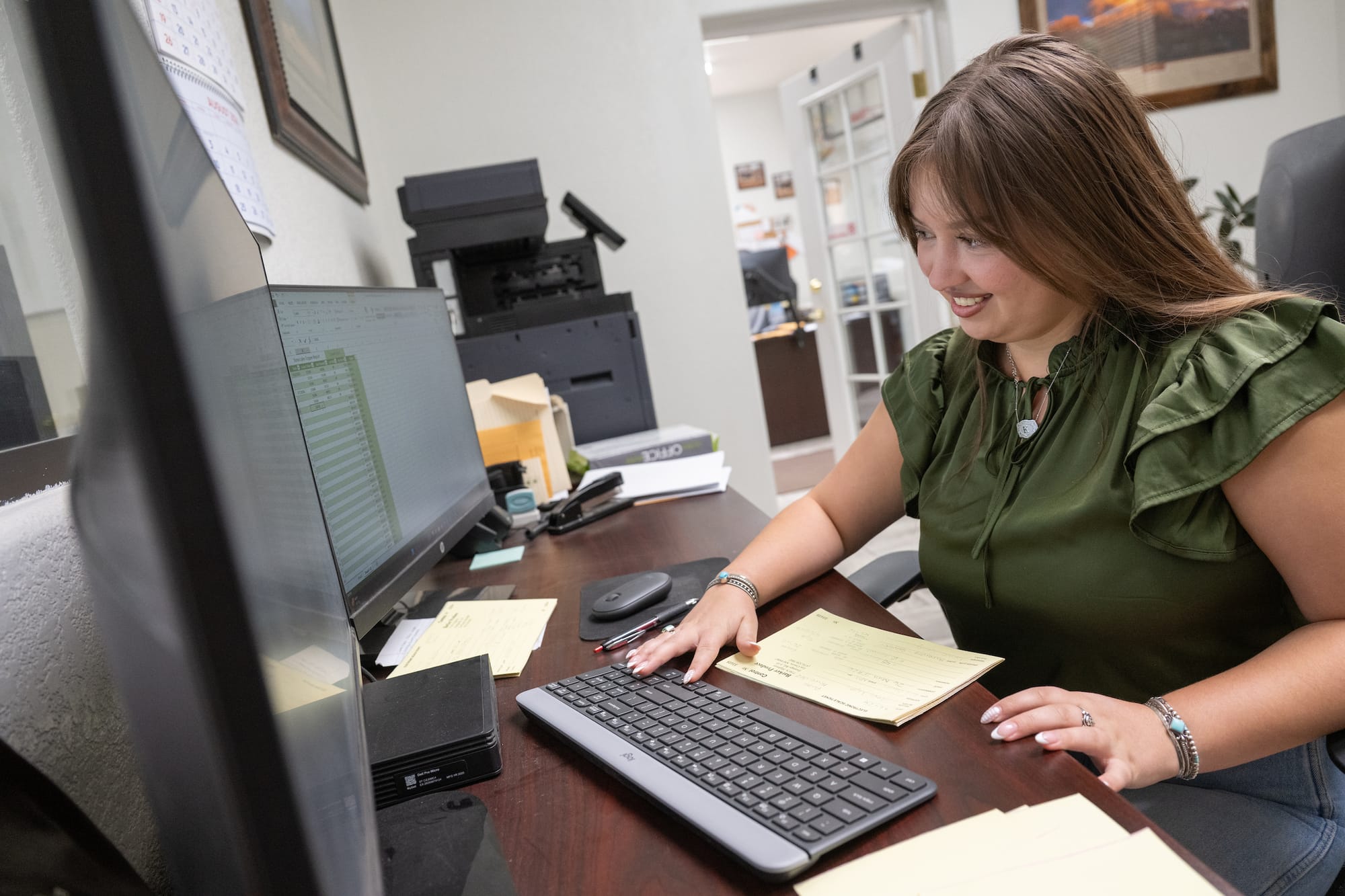 NMSU junior Kasi Montoya reviews a spreadsheet and paperwork at a computer during her internship at Barker Produce.