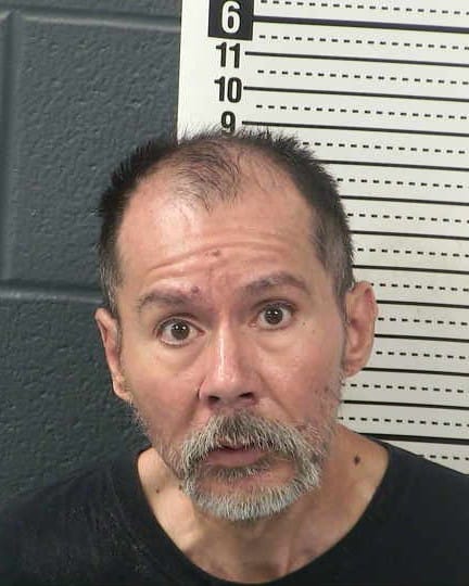 Booking photo of Aaron Padilla, 52, with short dark hair and a gray beard, wearing a black shirt.