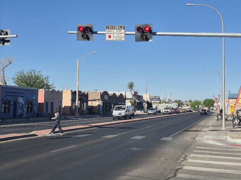 A pedestrian crosses Main Street in downtown Las Cruces as vehicles travel through the intersection beneath traffic signals.