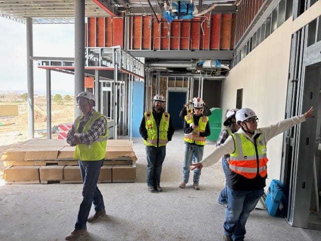 Workers in hard hats and safety vests stand beneath a covered exterior walkway at the new Doña Ana County Office of Emergency Management facility.
