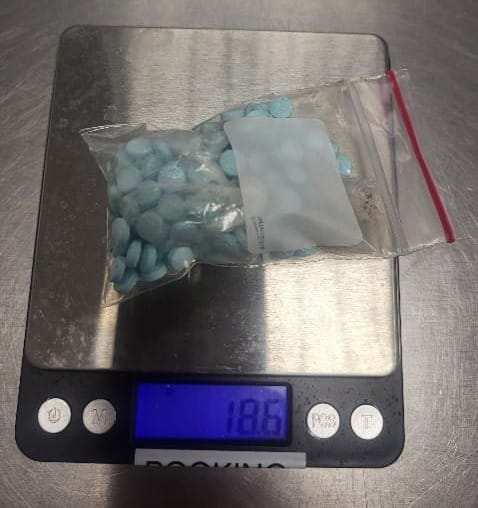 A clear plastic bag filled with blue pills sits on a digital scale reading 18.6 grams.