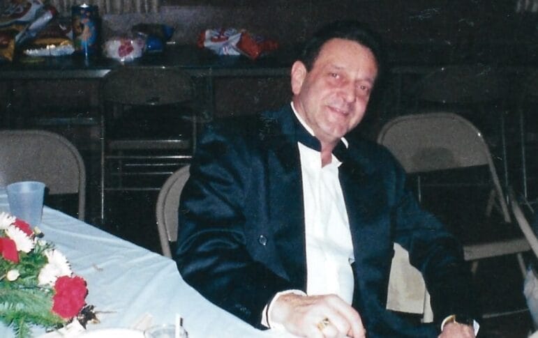 Joe Koslik sits at a table wearing a dark jacket over a white shirt in a family photograph.