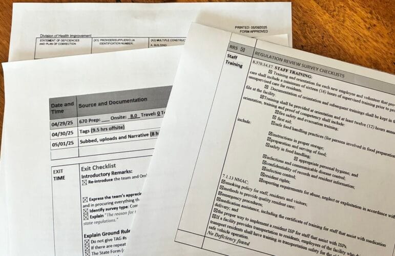 New Mexico Health Care Authority inspection survey forms are spread across a wooden table, showing checklists, training requirements and handwritten or typed survey notes.