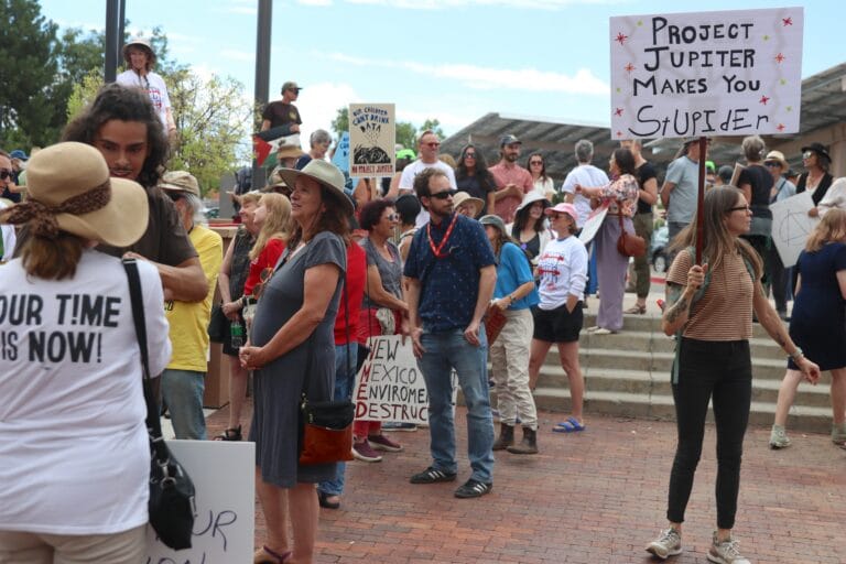 Protesters gather outside the New Mexico Environment Department in Santa Fe on Aug. 21, with one holding a sign reading “Project Jupiter makes you stupider.”