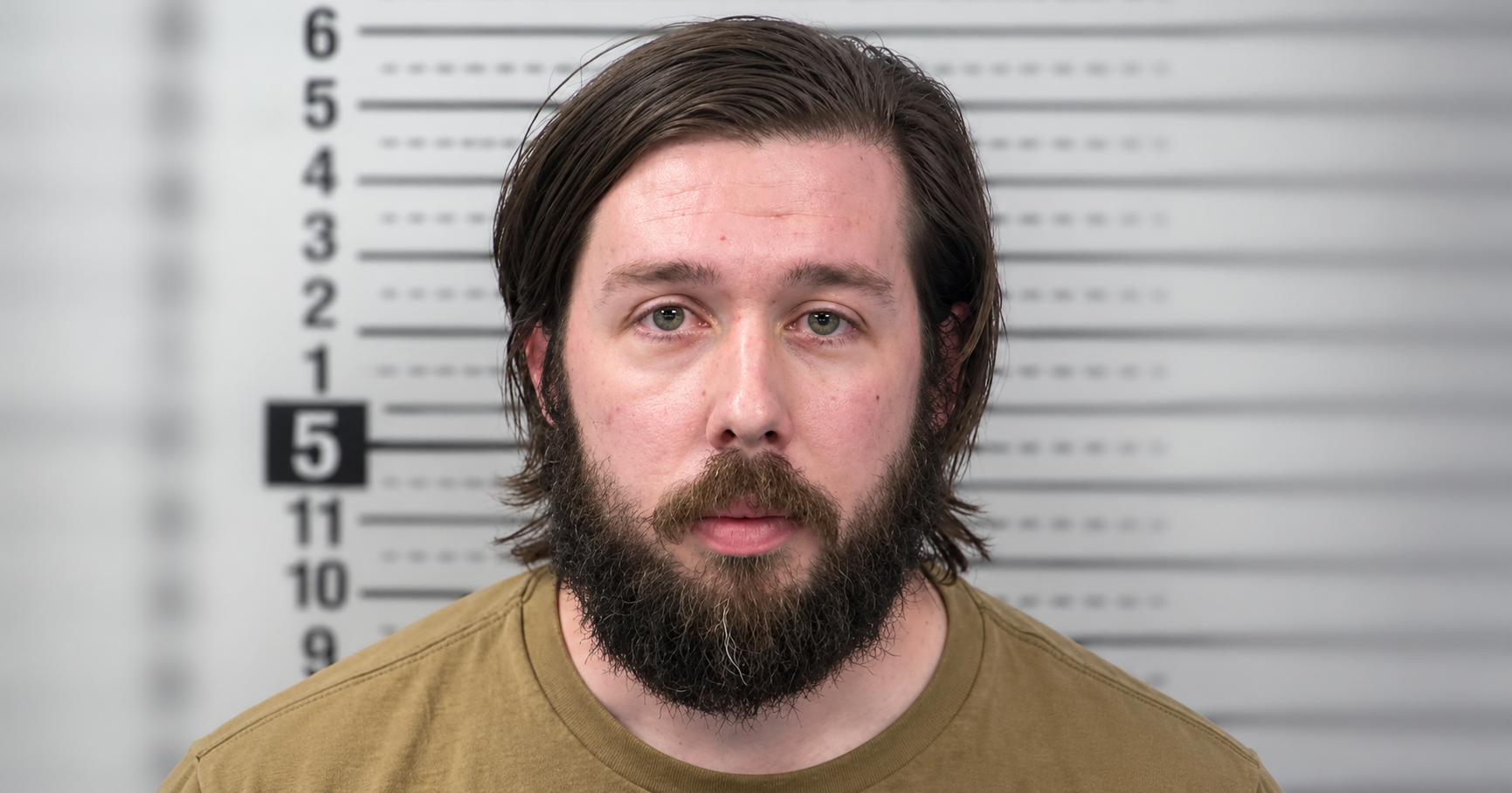 Booking photo of Christopher Lininger wearing a tan shirt, with medium-length brown hair and a full beard, against a blurred height-measurement backdrop.