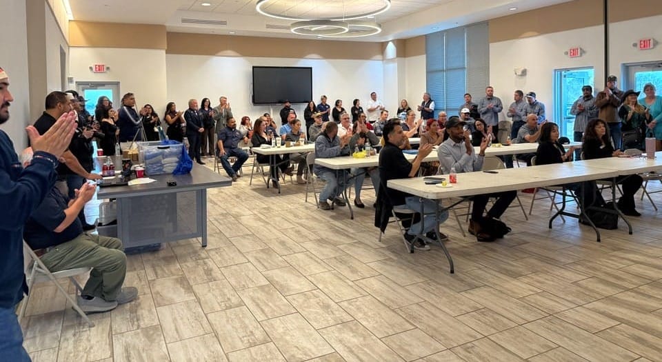 Attendees seated at tables and standing around a meeting room applaud during the Oct. 29, 2026, Weatherization Day celebration in Anthony, New Mexico.