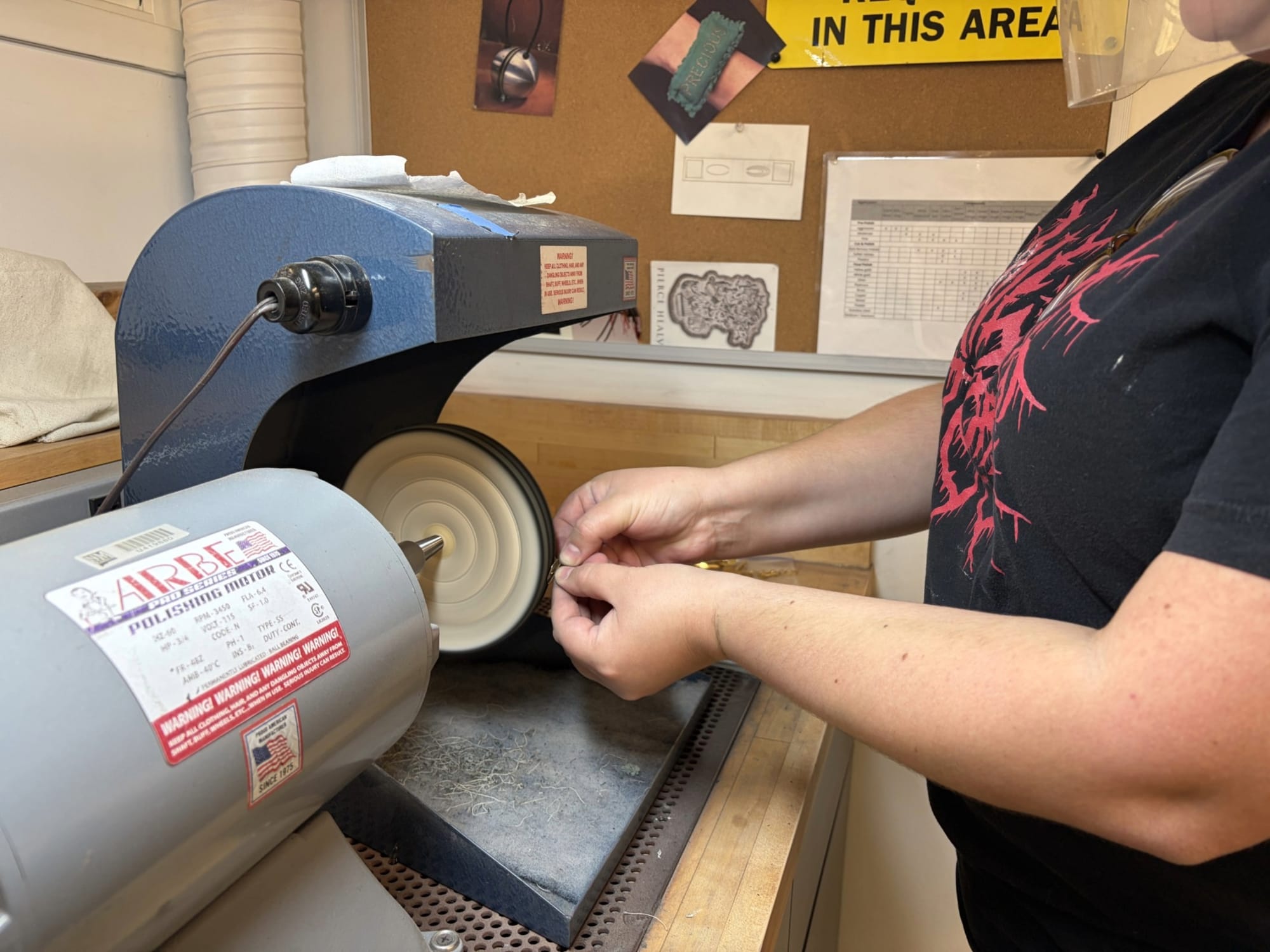 Crystal Evans holds a small jewelry piece against a spinning polishing wheel in NMSU's metalsmithing workshop while preparing for the annual jewelry sale.