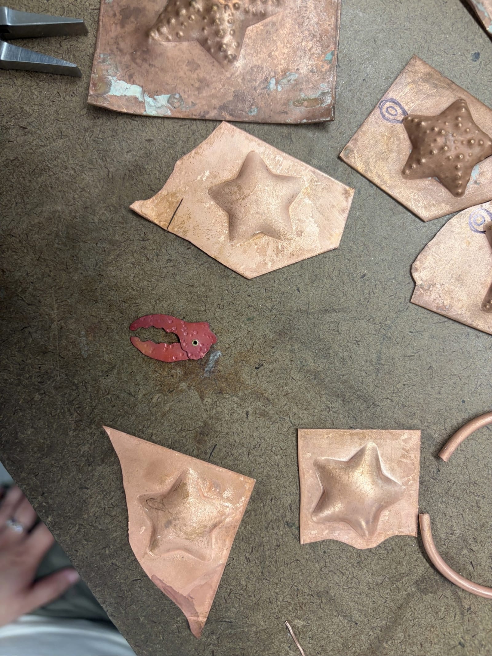 Copper sheets embossed with raised star shapes and a small red crab claw made by Olivia Novello are arranged on a worktable for NMSU's annual jewelry sale.