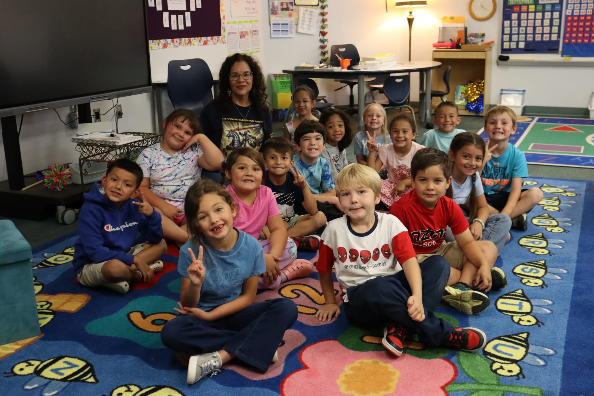 Nancy Orta poses with a group of first-grade students seated on a colorful classroom rug at East Picacho Elementary School in Las Cruces.