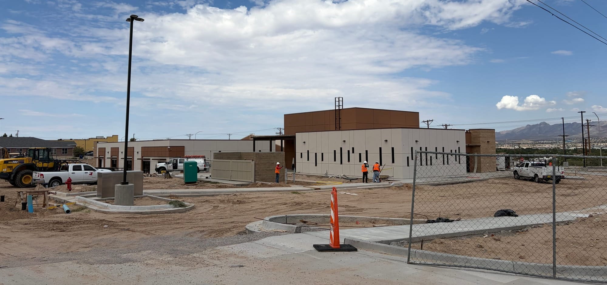 Wide view of the new Sunland Park food pantry under construction, with workers in safety vests, construction vehicles and fencing surrounding the building on McNutt Road.