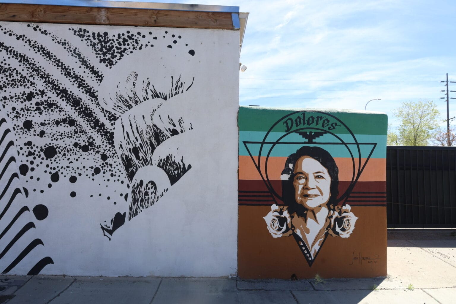 A colorful mural honoring Dolores Huerta depicts her portrait with roses against green, orange and brown stripes on a wall in Albuquerque.