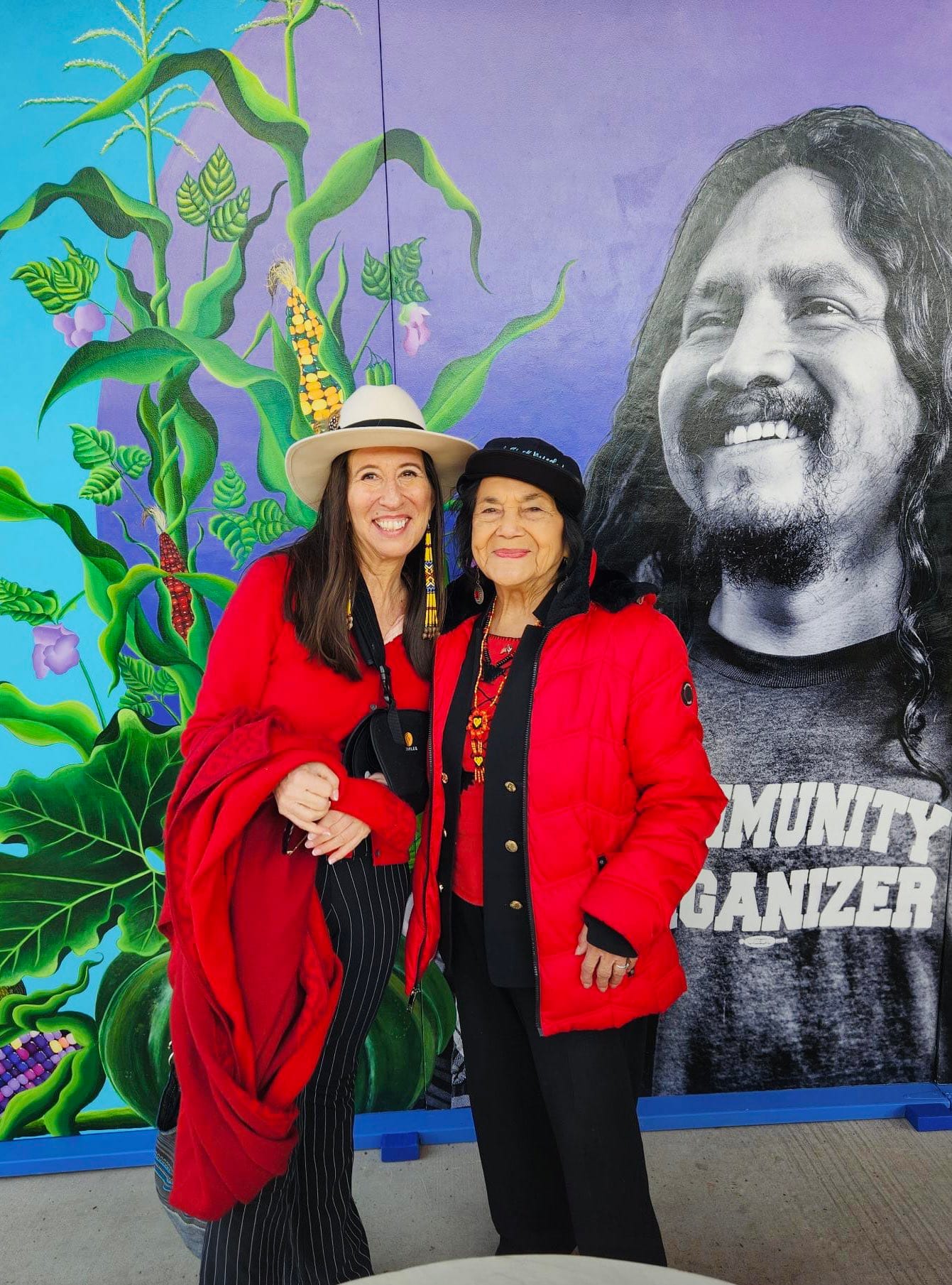 U.S. Rep. Teresa Leger Fernández and Dolores Huerta stand together in front of a colorful mural featuring plants and a large black-and-white portrait.