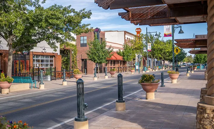 View of downtown Las Cruces, with tree-lined sidewalks, storefronts, benches and flower planters along Main Street.
