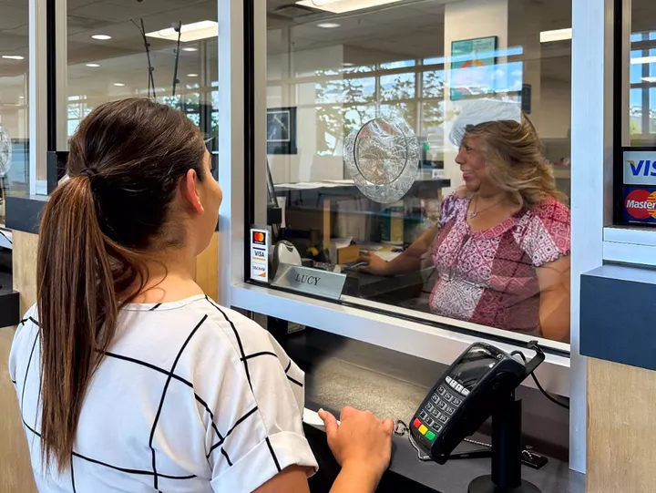A customer stands at a cashier’s window inside Las Cruces City Hall while a staff member assists from behind the glass.