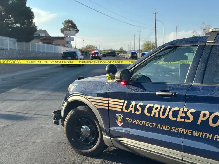 Las Cruces police vehicle blocks a street with crime scene tape stretched across the roadway during an investigation